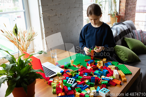 Image of Girl playing with constructor at home, watching teacher\'s tutorial on laptop. Digitalization, remote education