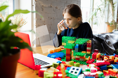 Image of Girl playing with constructor at home, watching teacher\'s tutorial on laptop. Digitalization, remote education