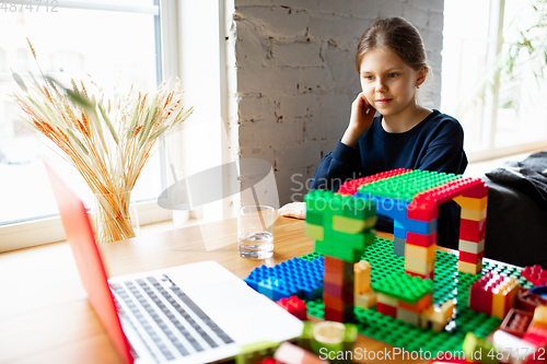 Image of Girl playing with constructor at home, watching teacher\'s tutorial on laptop. Digitalization, remote education