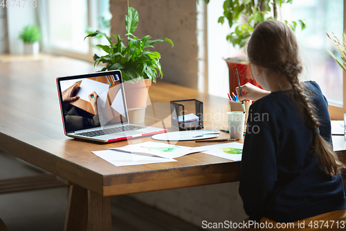 Image of Girl drawing with paints and pencils at home, watching teacher\'s tutorial on laptop. Digitalization, remote education