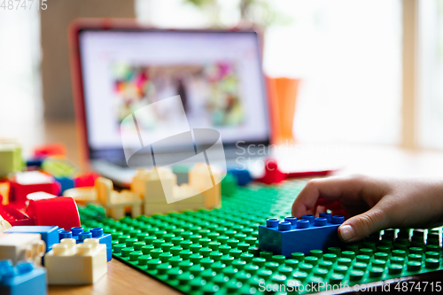 Image of Girl playing with constructor at home, watching teacher\'s tutorial on laptop. Digitalization, remote education