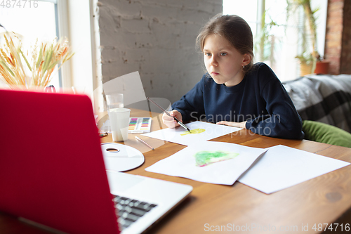 Image of Girl drawing with paints and pencils at home, watching teacher\'s tutorial on laptop. Digitalization, remote education