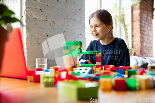 Image of Girl playing with constructor at home, watching teacher\'s tutorial on laptop. Digitalization, remote education