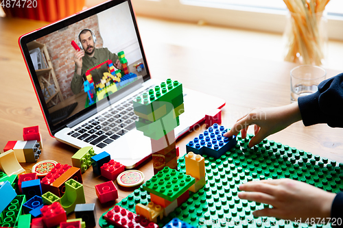 Image of Girl playing with constructor at home, watching teacher\'s tutorial on laptop. Digitalization, remote education