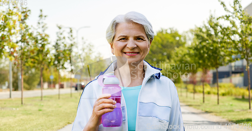 Image of sporty senior woman with bottle of water at park