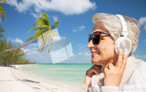 Image of old woman in headphones listens to music on beach