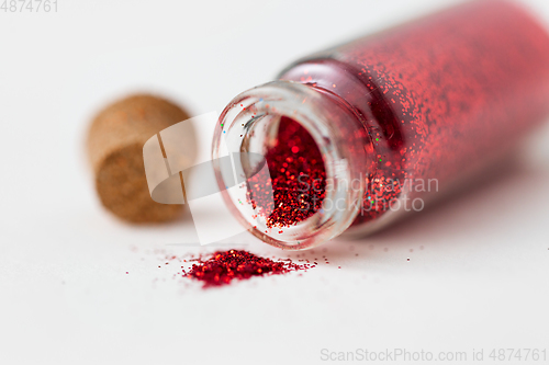 Image of red glitters poured from small glass bottle