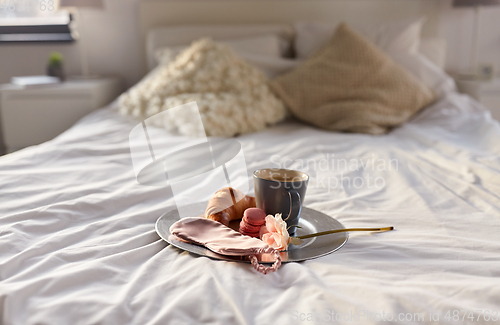 Image of croissant, coffee and eye sleeping mask in bed