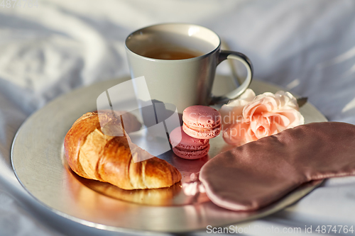 Image of croissant, coffee and eye sleeping mask in bed