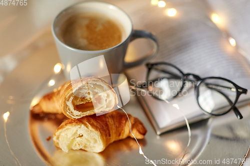 Image of croissants, cup of coffee, book and glasses in bed