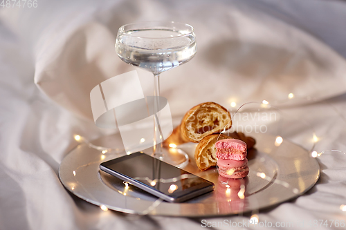 Image of champagne glass, croissants and smartphone in bed