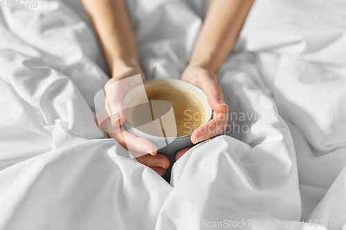 Image of hands of woman with cup of coffee in bed