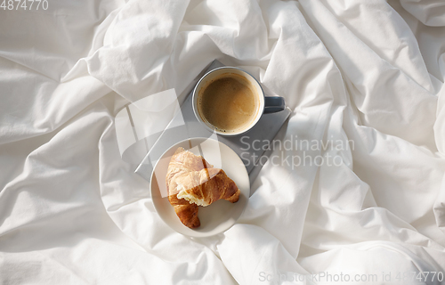 Image of croissants, cup of coffee and book in bed at home