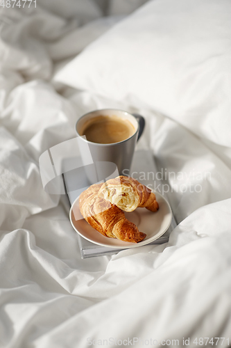 Image of croissants, cup of coffee and book in bed at home