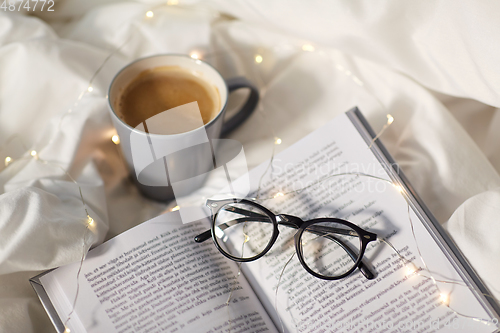 Image of cup of coffee, book, glasses and garland in bed