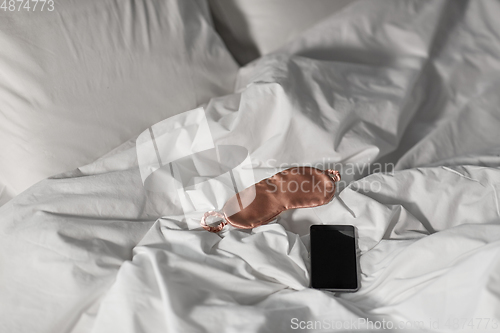 Image of smartphone and eye sleeping mask in bed at night