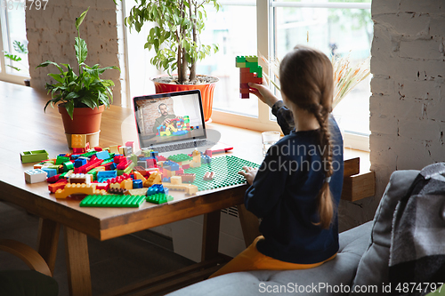 Image of Girl playing with constructor at home, watching teacher\'s tutorial on laptop. Digitalization, remote education