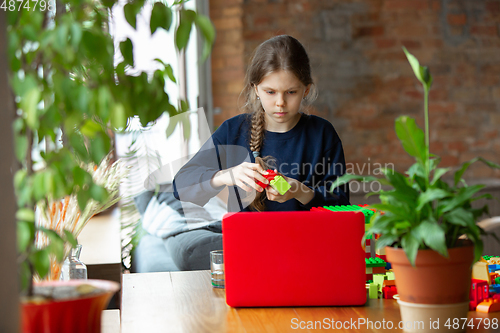 Image of Girl playing with constructor at home, watching teacher\'s tutorial on laptop. Digitalization, remote education