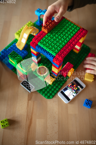 Image of Close up of male hands playing with colorful plastic constructor on wooden background