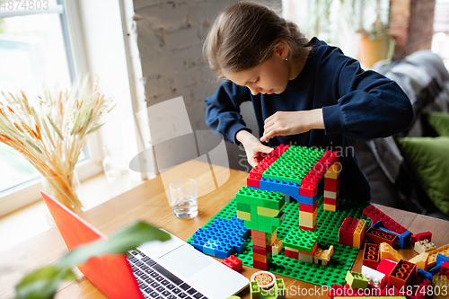 Image of Girl playing with constructor at home, watching teacher\'s tutorial on laptop. Digitalization, remote education