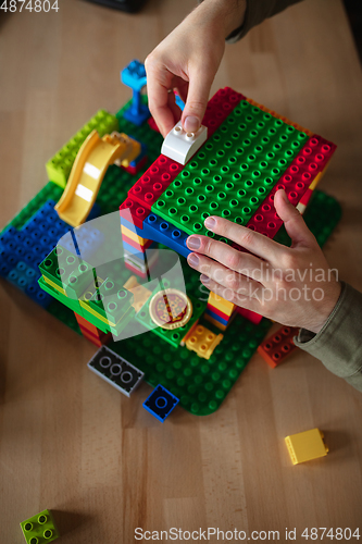 Image of Close up of male hands playing with colorful plastic constructor on wooden background