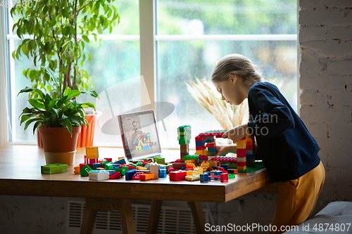 Image of Girl playing with constructor at home, watching teacher\'s tutorial on laptop. Digitalization, remote education