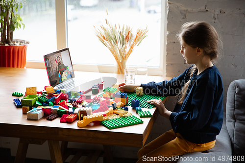 Image of Girl playing with constructor at home, watching teacher\'s tutorial on laptop. Digitalization, remote education