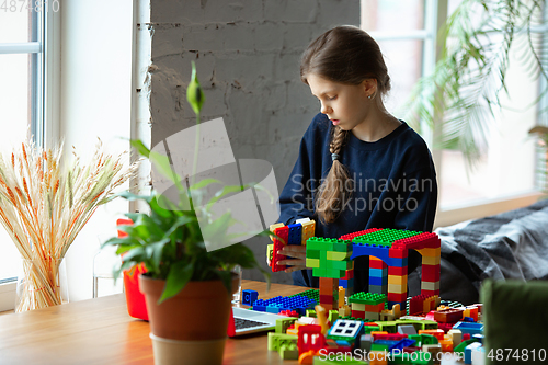 Image of Girl playing with constructor at home, watching teacher\'s tutorial on laptop. Digitalization, remote education