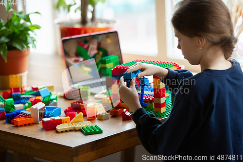 Image of Girl playing with constructor at home, watching teacher\'s tutorial on laptop. Digitalization, remote education