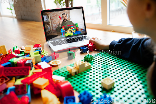 Image of Girl playing with constructor at home, watching teacher\'s tutorial on laptop. Digitalization, remote education