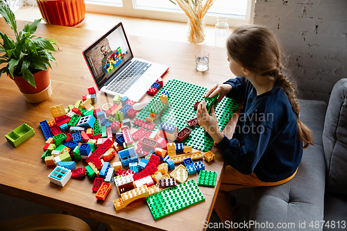 Image of Girl playing with constructor at home, watching teacher\'s tutorial on laptop. Digitalization, remote education