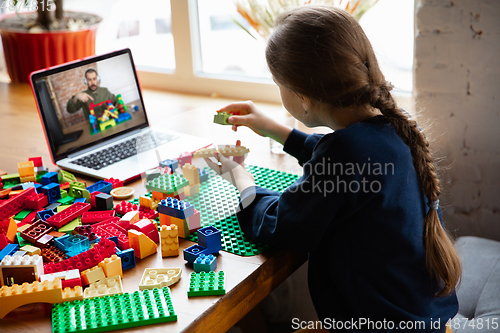 Image of Girl playing with constructor at home, watching teacher\'s tutorial on laptop. Digitalization, remote education