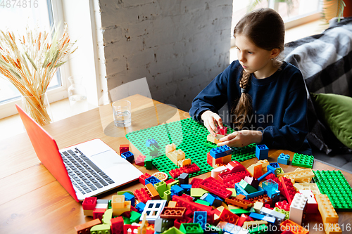 Image of Girl playing with constructor at home, watching teacher\'s tutorial on laptop. Digitalization, remote education