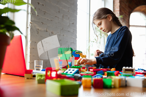 Image of Girl playing with constructor at home, watching teacher\'s tutorial on laptop. Digitalization, remote education