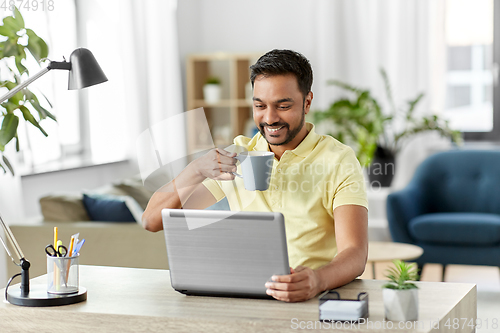 Image of man with laptop drinking coffee at home office