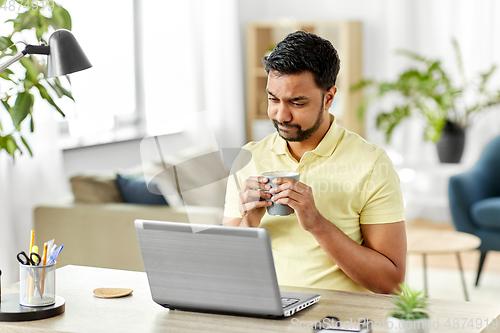 Image of man with laptop drinking coffee at home office