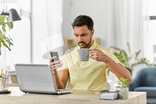 Image of man with smartphone drinking coffee at home office