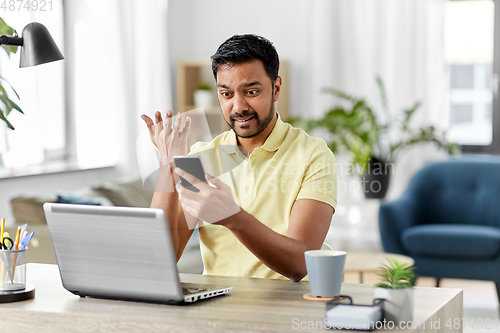 Image of angry indian man with smartphone at home office