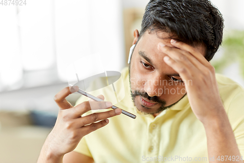 Image of stressed man with earphones calling on smartphone