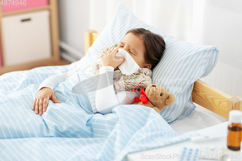 Image of sick girl lying in bed and blowing nose at home