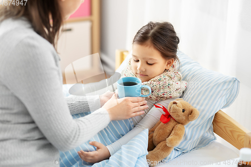 Image of mother giving hot tea to sick little daughter