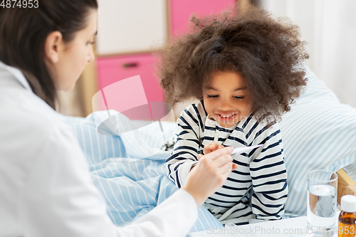 Image of doctor showing thermometer to smiling sick girl