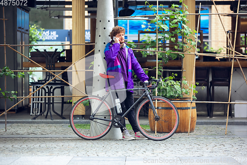 Image of Handsome young man using mobile phone and headphones while standing near his bicycle beside him