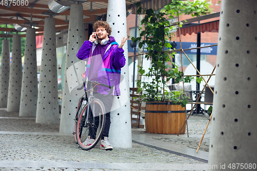 Image of Handsome young man using mobile phone and headphones while standing near his bicycle beside him