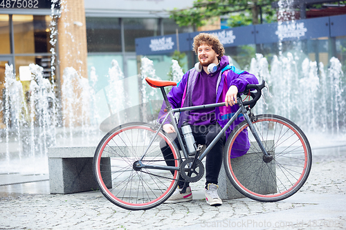 Image of Handsome young man using headphones while sitting near his bicycle beside him