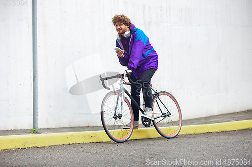 Image of Handsome young man using mobile phone and headphones while riding his bicycle