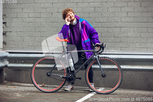 Image of Handsome young man using mobile phone and headphones while standing near his bicycle beside him