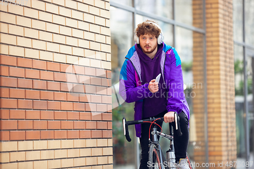 Image of Handsome young man using mobile phone and headphones while riding his bicycle