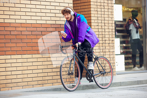 Image of Handsome young man using mobile phone and headphones while riding his bicycle