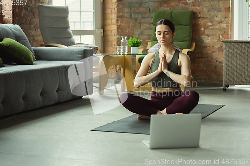 Image of Sporty young woman taking yoga lessons online and practice at home